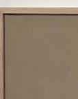 close-up of a framed wall art piece with a textured taupe-brown panel and a light natural wood frame against a white wall.