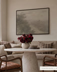 forgotten road in a black floater frame above a sunlit breakfast nook with a linen banquette, a round marble pedestal table, a vase of deep red flowers, and wooden armchairs with leather seats. shown in floater black, 48 x 36. __lifestyleimage