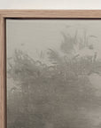 close-up of the top corner of forgotten road in a light oak floater frame against a white wall, showing the canvas edge and a dark stand of trees softened by fog.