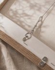 close-up of a framed canvas or fabric artwork showing the wooden frame, metal hanging hardware, and textured off-white fabric with soft leaf shadows.