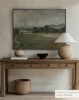 wooden console table with decorative items against a wall with a landscape painting.