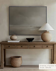 wooden console table with decorative items against a beige wall with a framed artwork.