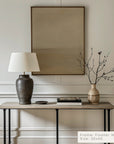decorative table with lamp, vase, and branches against a wall with a framed picture.