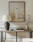 decorative interior setting with a table, lamp, and vase against a wall with framed art.