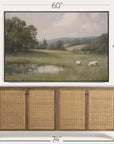 framed landscape painting of a field with sheep above a wooden cabinet.