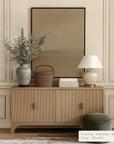 wooden sideboard with decorative items against a beige wall with a framed artwork.