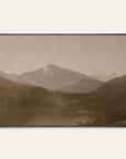 white mountains art print in a black floater frame. a pale mountain peak rises over dark wooded hills and a still lake in warm sepia tones, shown against a plain off-white wall.
