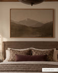 a closer view of white mountains in a light oak floater frame above an upholstered bed with floral pillows and a plum lumbar pillow, under a dark pendant light. shown in floater oak, 60 x 40.