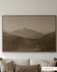 white mountains in a light oak floater frame on a sunlit white wall above a cream sofa with floral, striped, and olive green pillows. shown in floater oak, 60 x 40.
