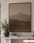 white mountains in a dark walnut floater frame above a cream plaster console with olive branches in a dark vase, a wooden bowl on books, and brass candlesticks. shown in floater walnut, 36 x 48.