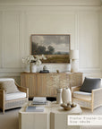 modern living room with wicker chairs, a coffee table, and a framed landscape painting on the wall.