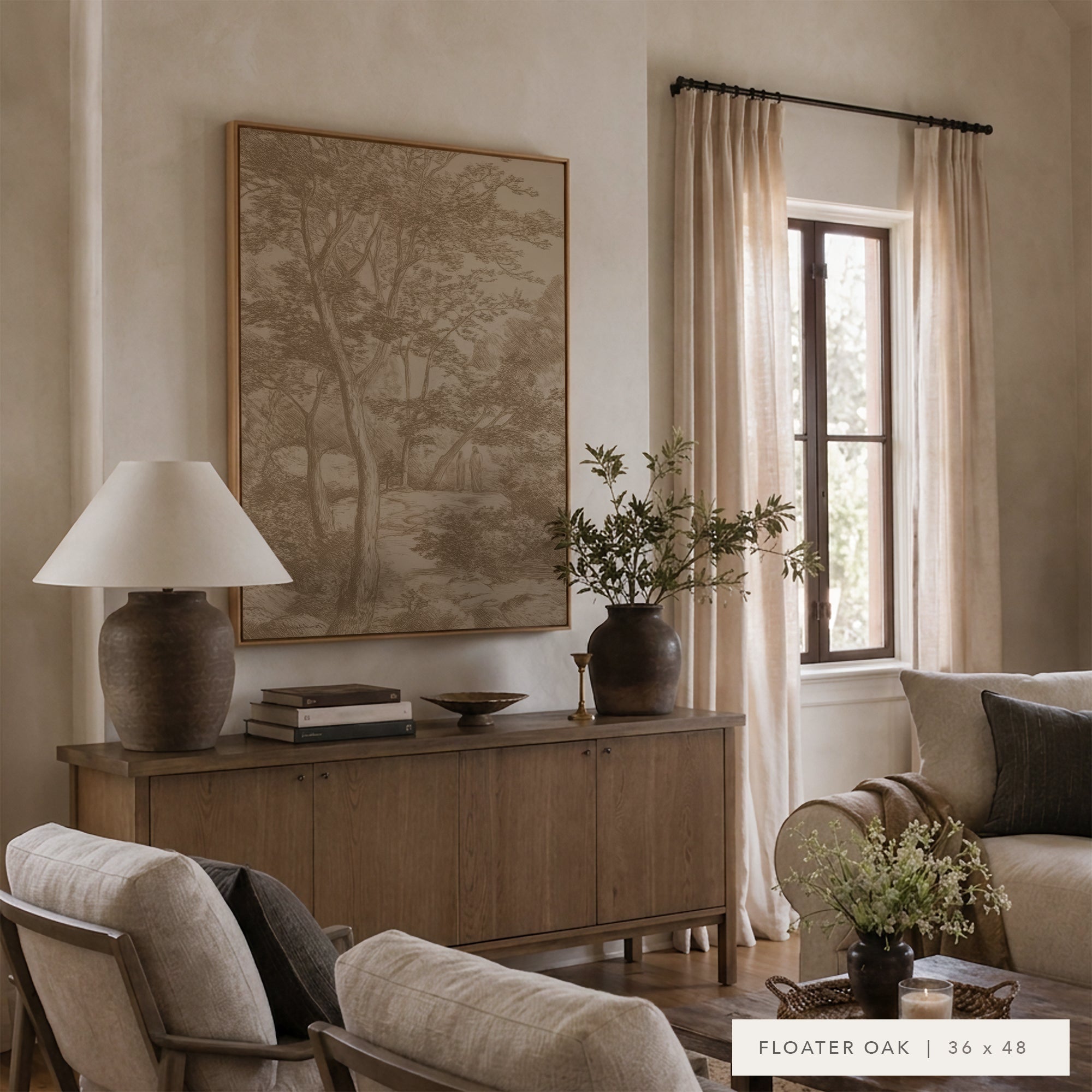 A framed landscape art print in a warm wood frame hangs on a beige wall above a wooden credenza in a styled living room. The print depicts a serene forest scene in muted earthy tones.
