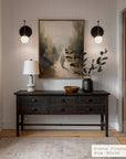 narrow hallway with a dark wooden console table, lamp, and painting on a white wall.