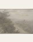 forgotten road art print in a gold floater frame. a foggy road fades past a dark stand of trees in soft grays and warm stone tones, shown against a plain off-white wall. 