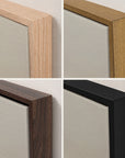 four-panel close-up of the top corner of the vertical forgotten road print in each floater frame finish: light oak, gold, walnut, and black, hung against an off-white wall, with the soft gray fog of the artwork inside.