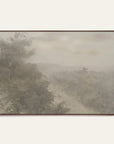 forgotten road art print in a dark walnut floater frame. a foggy road fades past a dark stand of trees in soft grays and warm stone tones, shown against a plain off-white wall. 