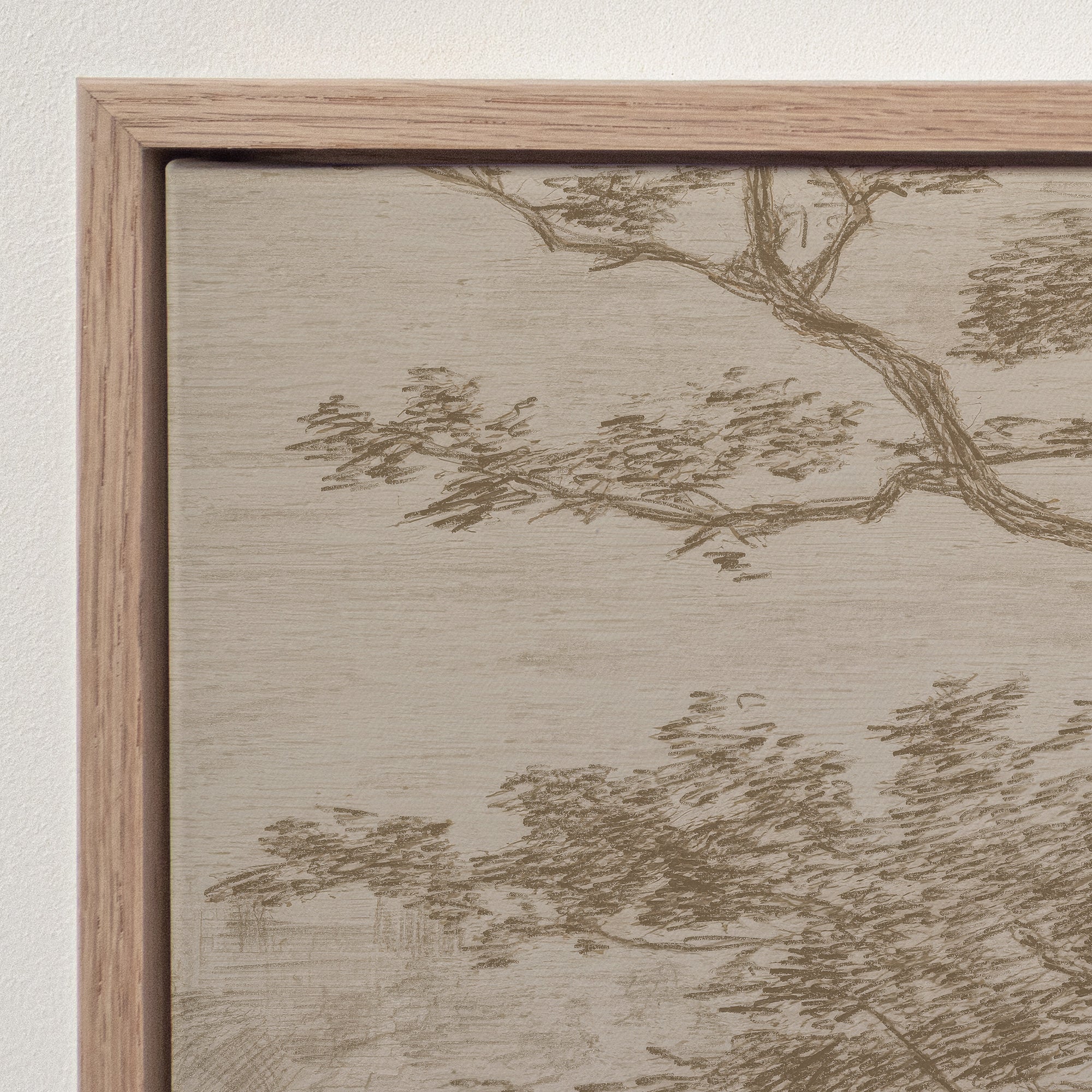 Close-up of a framed wall art print showing a beige and taupe landscape with tree branches and foliage, set in a light natural wood frame against a white wall.