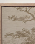 close-up of a framed wall art print showing a beige and taupe landscape with tree branches and foliage, set in a light natural wood frame against a white wall.
