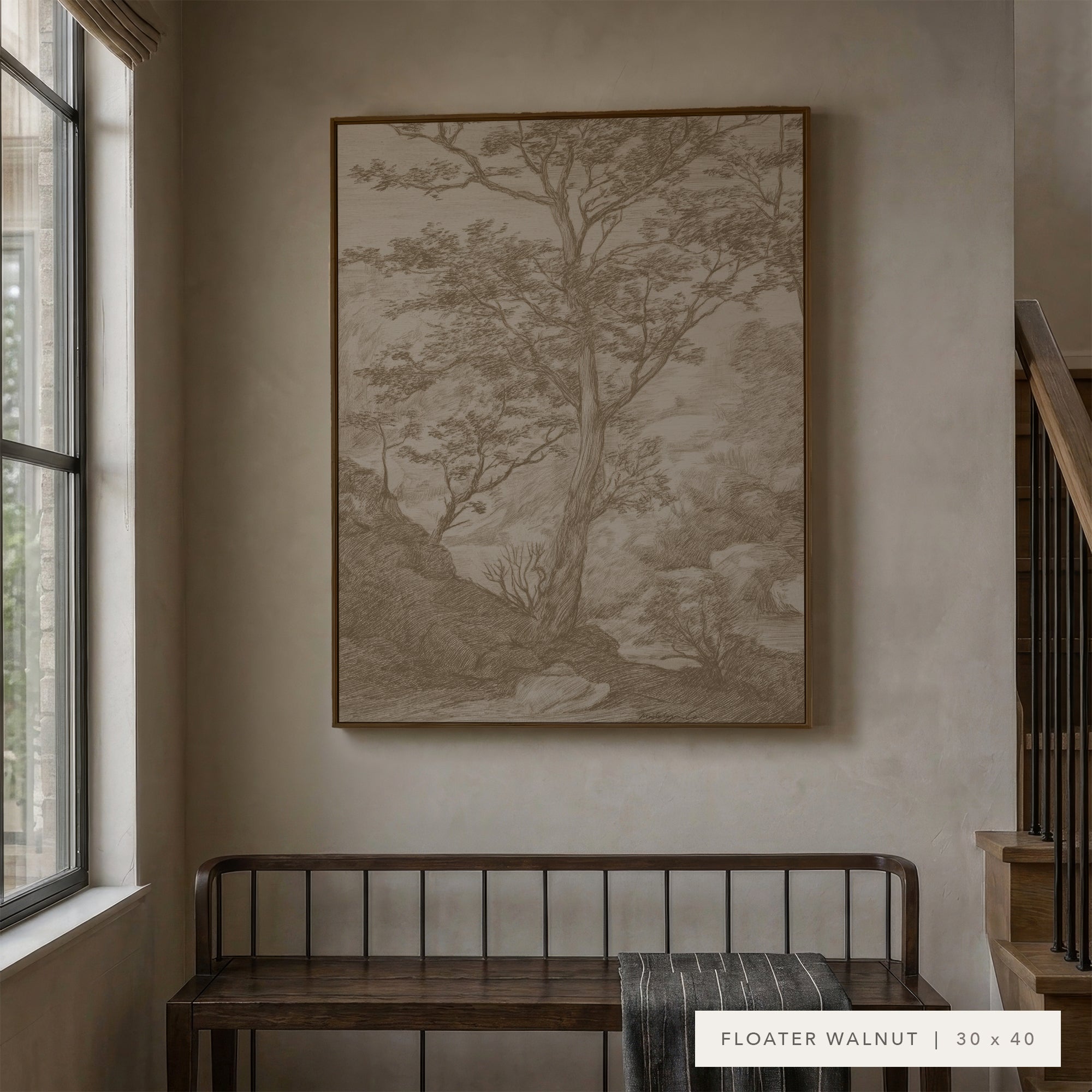 A framed landscape art print in a warm brown wood frame hangs on a textured beige wall above a dark wooden bench in a styled interior setting.