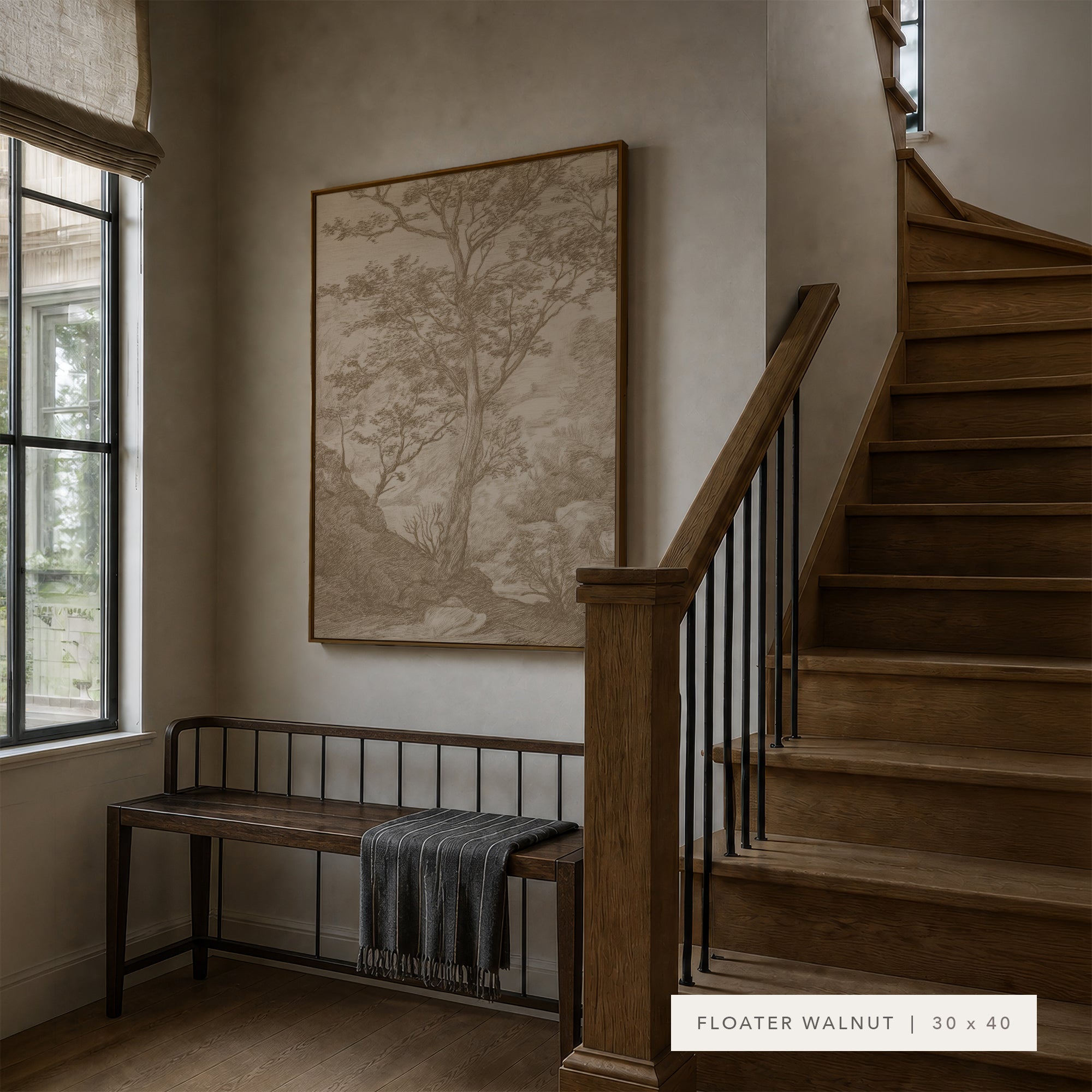 A large framed wall art print featuring a sepia-toned tree landscape hangs on a beige wall in a staircase landing. A dark wood bench with a gray throw sits below the artwork, and a wooden staircase with black metal railings is to the right.