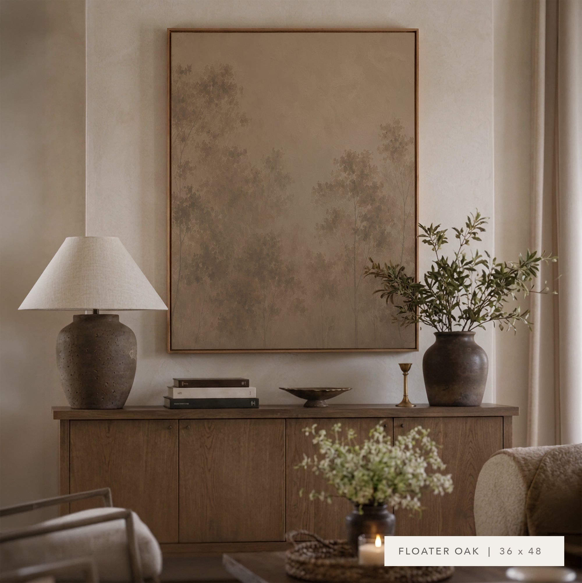 A large framed wall art print in a warm taupe and beige abstract landscape design, styled in a cozy living room setting above a wooden console table with a lamp, books, and a vase. __lifestyleImage