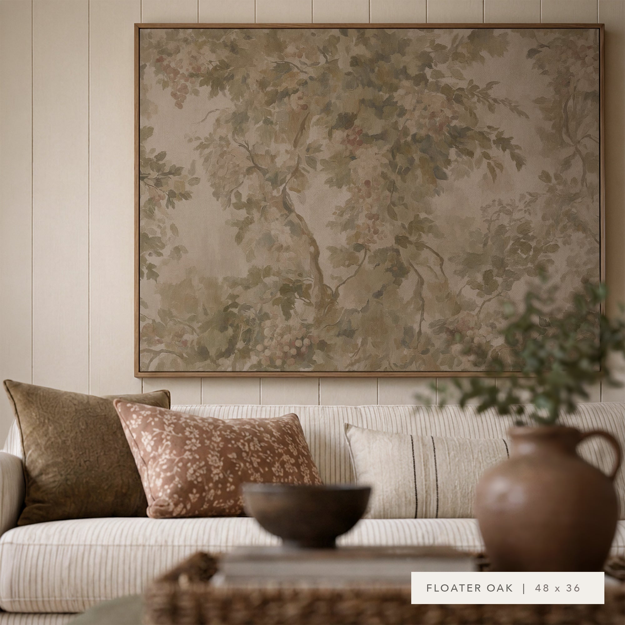 A large framed wall art print featuring a vintage-style botanical tree pattern in muted earthy tones, displayed above a cream sofa with patterned pillows in a styled living room. A small label in the bottom right reads 'FLOATER OAK | 48 x 36'.