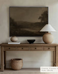 wooden console table with decorative items against a beige wall with a landscape painting.