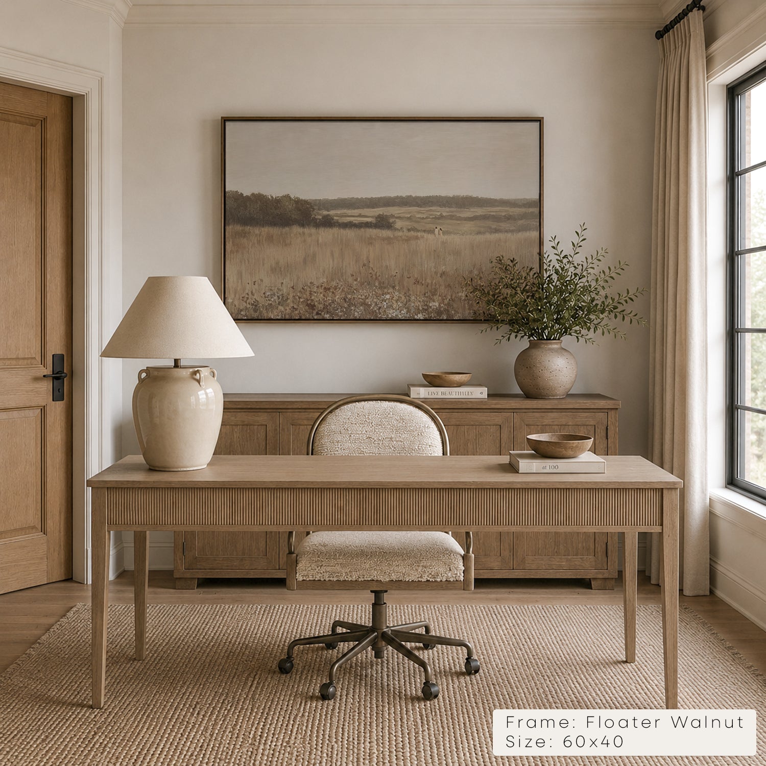 A framed landscape art print in a Floater Walnut frame hangs on a beige wall above a wooden console table in a styled home office. The print depicts a dry grass field under a soft sky. __lifestyleImage