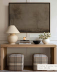 wooden console table with lamp, books, and flowers against a wall with a framed abstract painting.