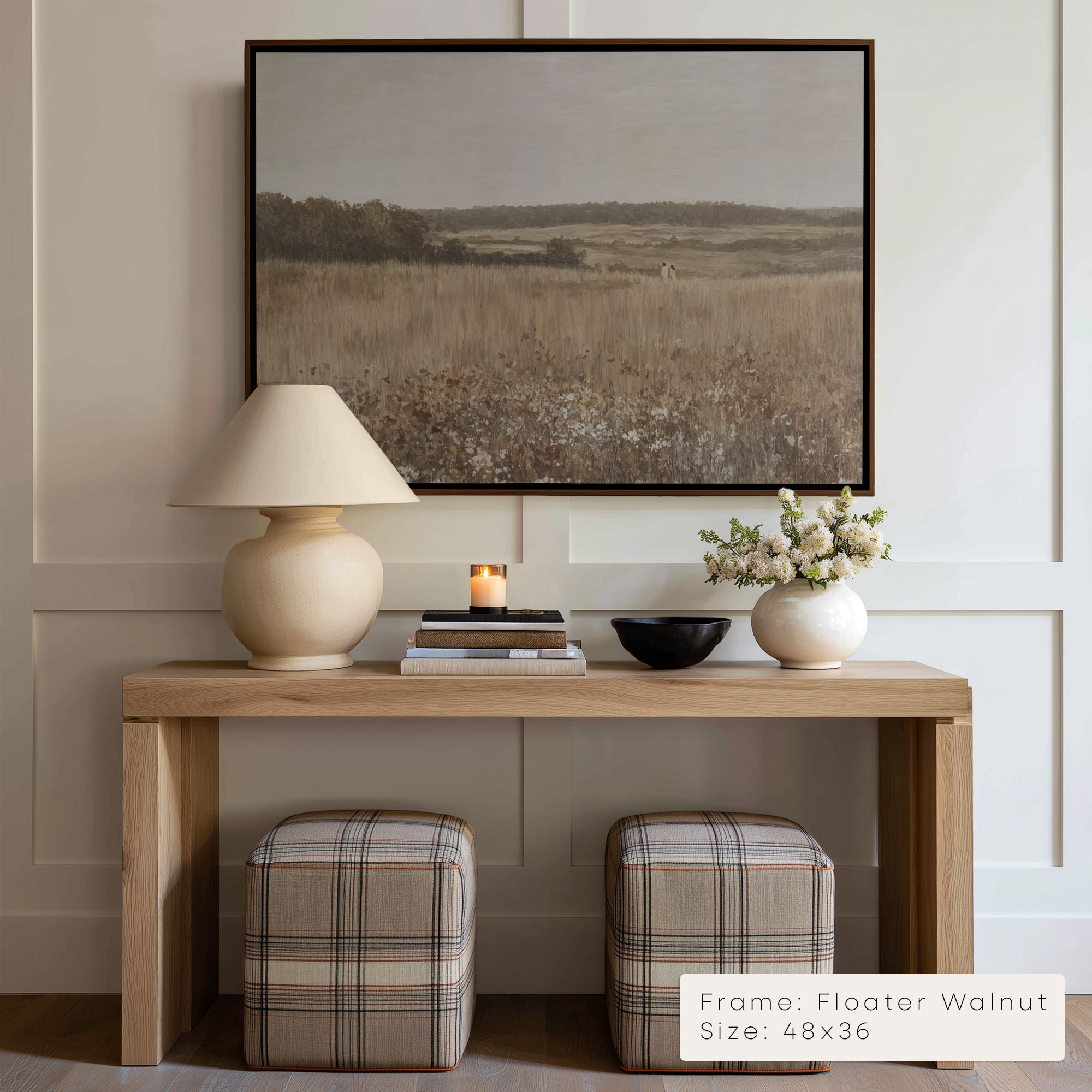Wooden console table with lamp, books, and flowers against a wall with a framed landscape painting.