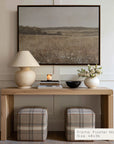 wooden console table with lamp, books, and flowers against a wall with a framed landscape painting.