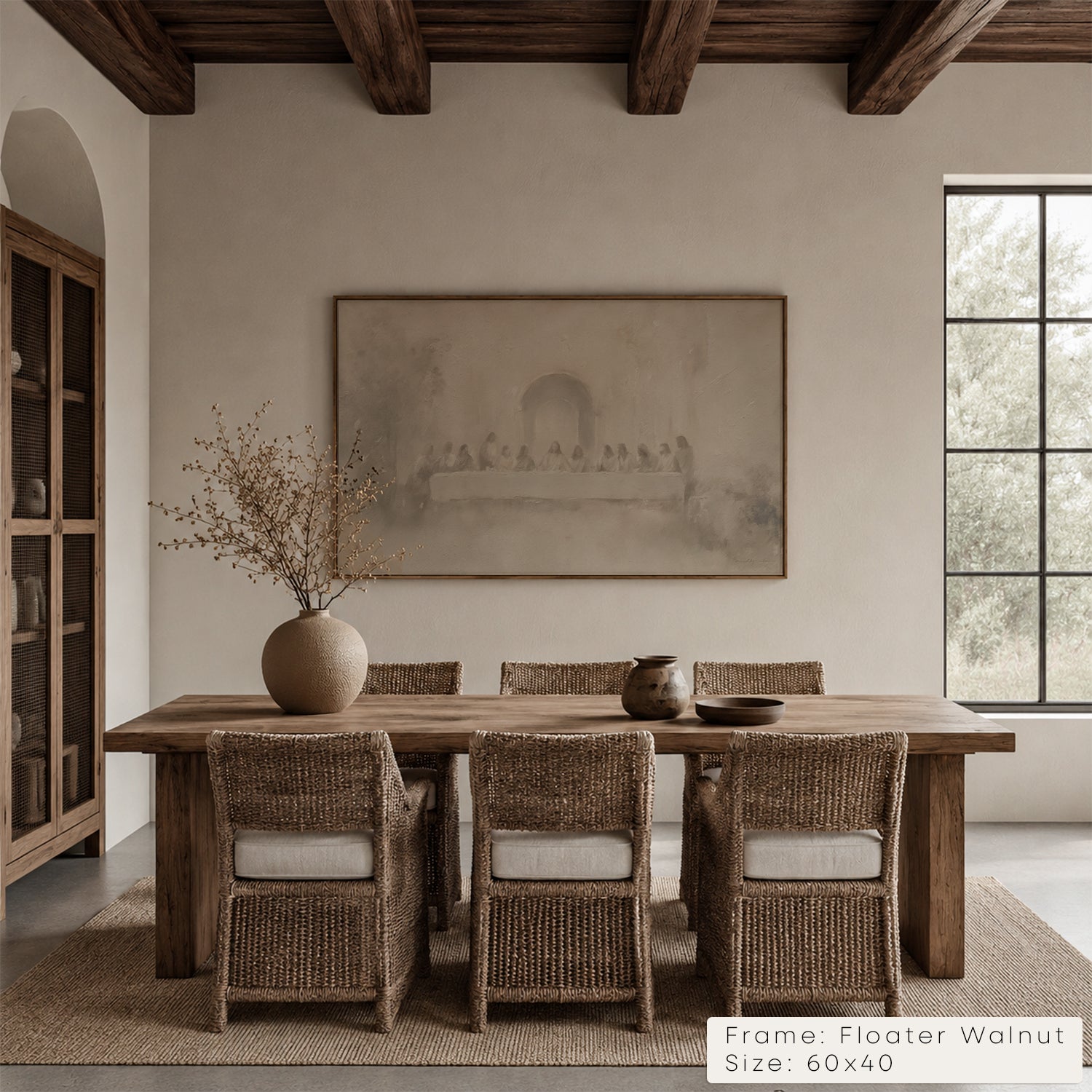 A large framed wall art print hangs above a rustic wooden dining table with woven chairs in a neutral dining room. The print depicts a soft sepia architectural scene. __lifestyleImage