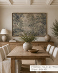 a large framed landscape art print hangs on a beige wall above a wooden dining table and chairs in a styled dining room. the print depicts a soft, muted forest scene in blue-gray, beige, and brown tones. __lifestyleimage