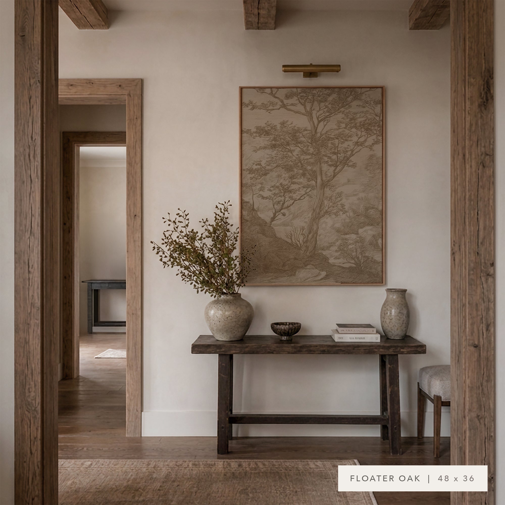 A framed landscape art print in a warm beige and brown tone hangs on a cream-colored wall above a rustic dark wood console table. The scene is styled with neutral ceramic vases, books, and dried botanicals, framed by rustic wooden doorposts. __lifestyleImage