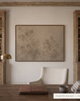 A framed art print featuring a minimalist beige and brown botanical design, displayed on a white wall in a styled home office setting with wooden bookshelves, a desk, and a chair.