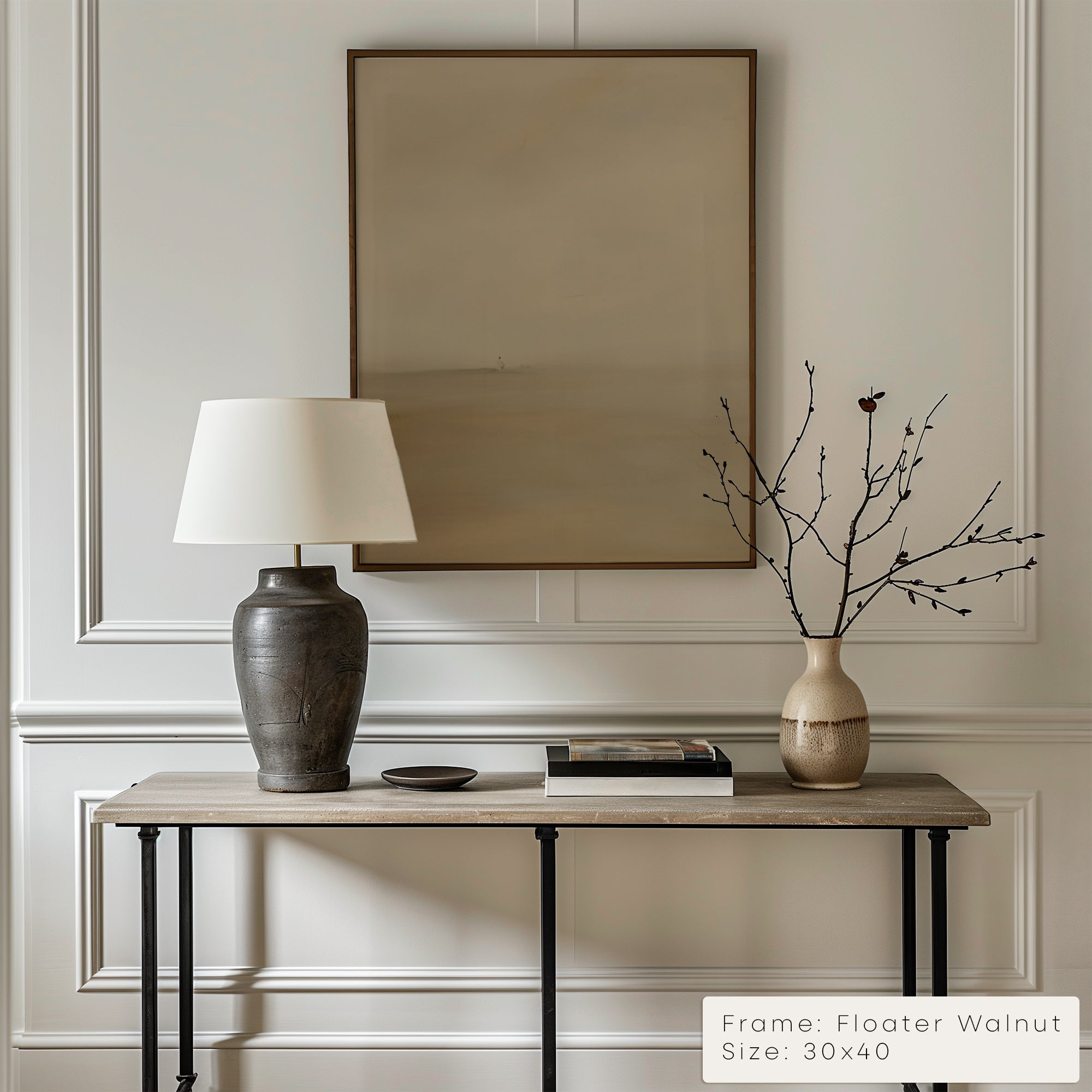Decorative table with lamp, vase, and branches against a wall with a framed picture.