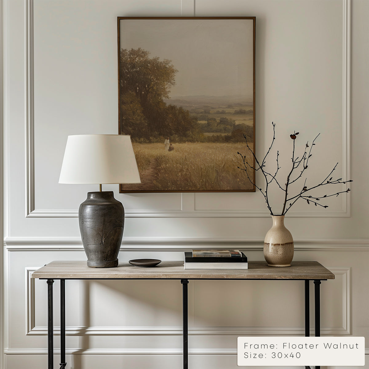 Decorative interior setting with a table, lamp, and vase against a wall with a framed landscape painting.