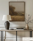 decorative interior setting with a table, lamp, and vase against a wall with a framed landscape painting.