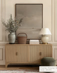 wooden sideboard with decorative items against a beige wall with a framed picture.