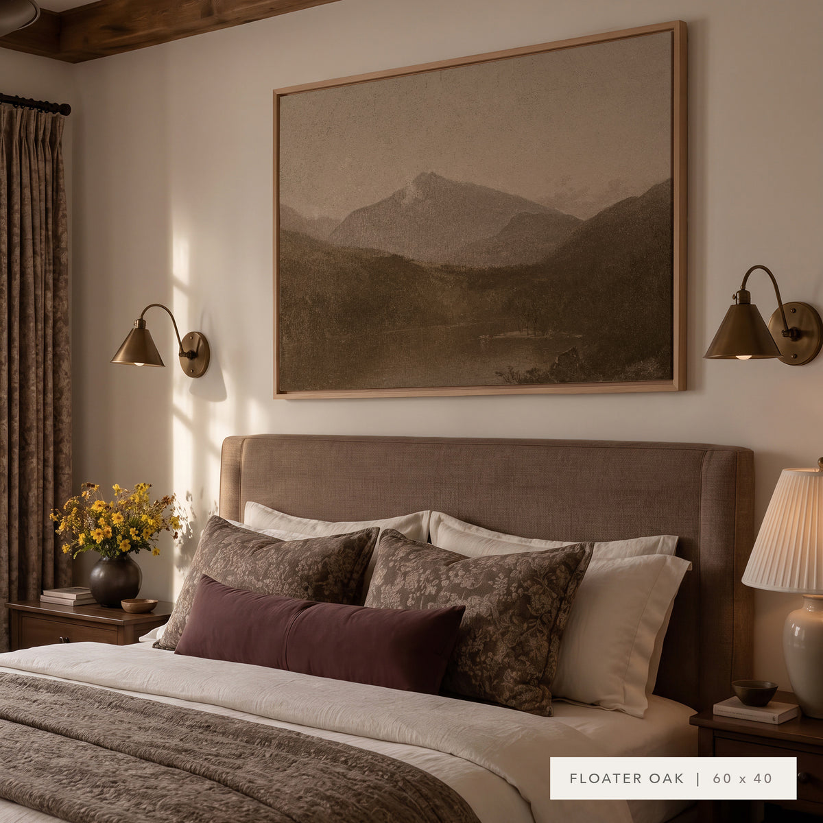 White Mountains in a light oak floater frame above an upholstered bed with floral and plum pillows, between two brass wall sconces, with yellow flowers on the nightstand. Shown in Floater Oak, 60 x 40. __lifestyleImage