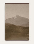 white mountains vertical art print in a dark walnut floater frame. a pale mountain peak rises over dark wooded hills and a still lake in warm sepia tones, shown against a plain off-white wall. 