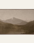 white mountains art print in a dark walnut floater frame. a pale mountain peak rises over dark wooded hills and a still lake in warm sepia tones, shown against a plain off-white wall. 